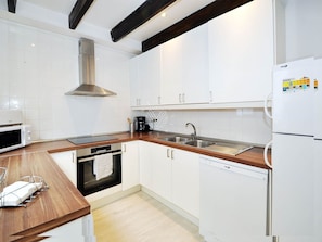 Una cocina moderna con gabinetes blancos, una campana extractora de acero inoxidable, horno empotrado, lavavajillas y refrigerador con panel de control.