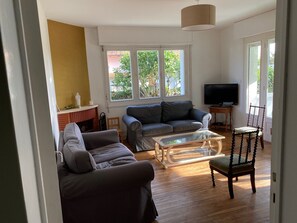 A living room with a sofa, a coffee table, a television, and a window with a view of greenery. - Single-story beachfront villa, very quiet, enclosed garden, beaches and shops within walking distance (Saint-Georges-de-Didonne)
