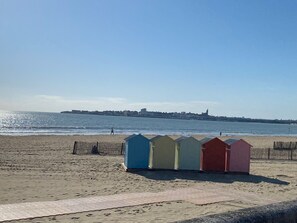 A beach with a row of colorful beach huts and a distant cityscape. - Single-story beachfront villa, very quiet, enclosed garden, beaches and shops within walking distance (Saint-Georges-de-Didonne)