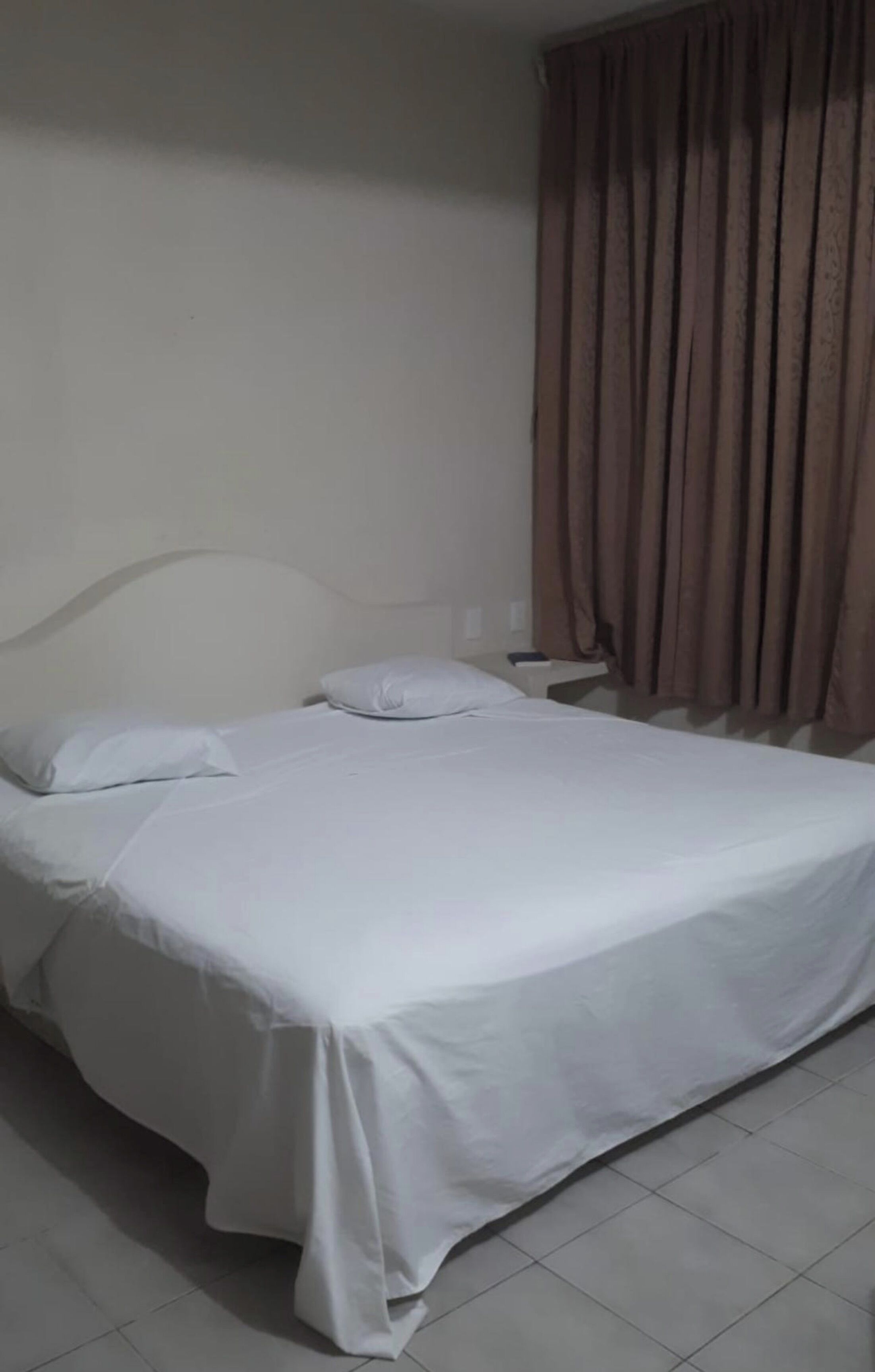 Ein Einzelbett mit weißer Bettwäsche in einem Zimmer mit schlichter Wand und einem Vorhang.
