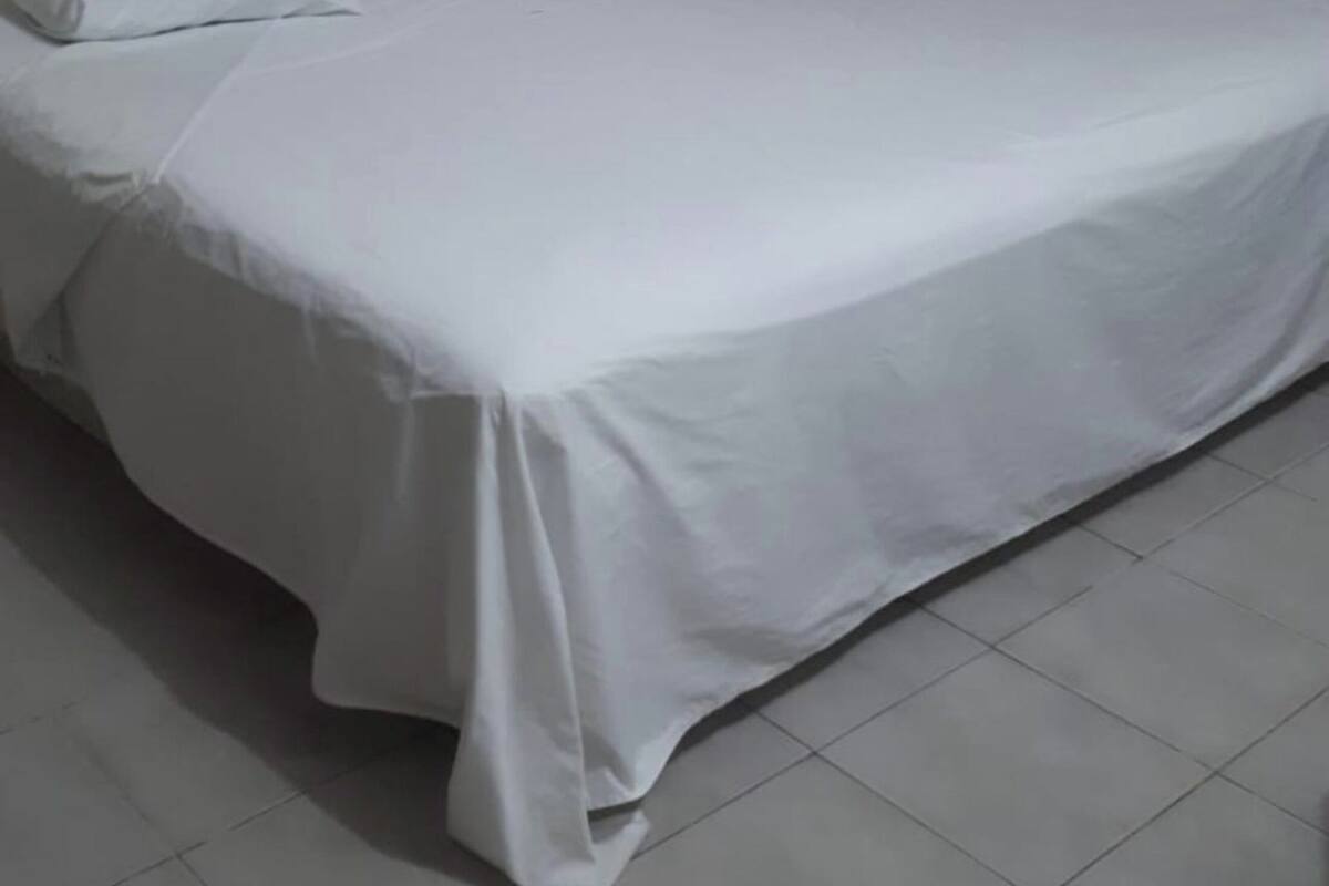 A single bed with white bedding in a room with a plain wall and a curtain.