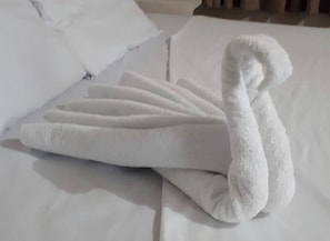 A neatly folded white towel on a bed with white bedding. - Diamantes Boutique (Acapulco)