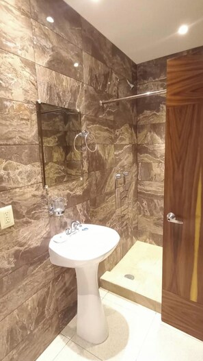 Ein Badezimmer mit einem Waschbecken auf Säule, einer Dusche mit Glastür und einer Holztür.