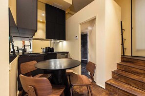 A modern kitchen with a round dining table and wooden chairs, a black countertop, and a staircase leading to another level. - JUST MOMENTS FROM LA MADELEINE, THE ICONIC FAUBOURG SAINT-HONORÉ (Paris)