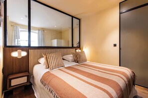 A bedroom with a large bed, a wooden nightstand, a mirror, and a wardrobe. - JUST MOMENTS FROM LA MADELEINE, THE ICONIC FAUBOURG SAINT-HONORÉ (Paris)