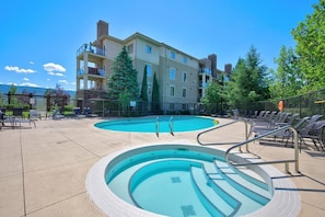 A swimming pool with steps, lounge chairs, and a building with balconies. - Mountain View Condo | Pool, Hot Tub & Golf Nearby 1207 (Kelowna)