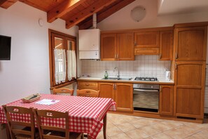 A kitchen with wooden cabinets, a tiled backsplash, a stove, and a table with a checkered tablecloth. - Vrbo Property (Mastellina)