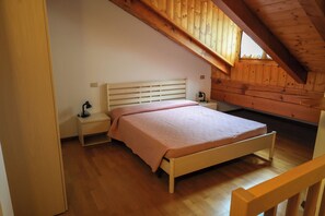 Een slaapkamer met een houten bed, nachtkastjes en een schuine kap.