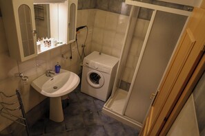 A bathroom with a sink, mirror, washing machine, and shower. - Vrbo Property (Mastellina)