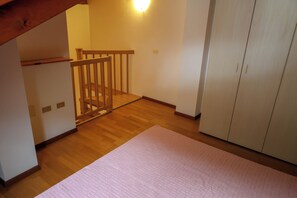 Een kamer met houten vloer, een witte kast, een roze vloerkleed en een houten leuning.