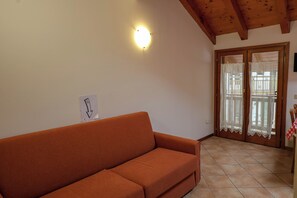 A room with a sofa, a ceiling light, a door with lace curtains, and a tiled floor. - Vrbo Property (Mastellina)