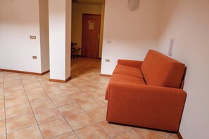 A room with a sofa, tiled floor, a door, and a wall-mounted light fixture. - Apartment 7 Maso Anna (Mastellina)