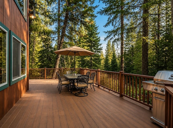 A wooden deck with a table and chairs, a grill, and a view of tall trees.