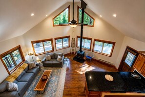 Een ruime loft met een hoge nok, grote ramen, een open haard en een eethoek.
