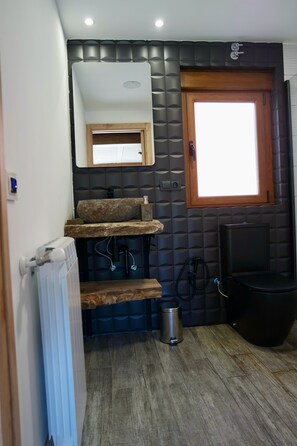 Een badkamer met een houten wastafelmeubel, een raam, een radiator en een zwarte prullenbak.