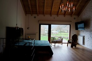 A room with a bed, a TV mounted on the wall, a wooden ceiling, and a view through a large window. - Quiet design duplex with mountain views (Villablino)