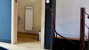 Porta in legno che dà su un bagno con termosifone, un quadro appeso al muro e un interruttore della luce bianco.