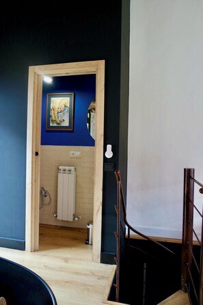 A wooden-framed doorway leading to a bathroom with a radiator, a framed picture on the wall, and a white light switch.