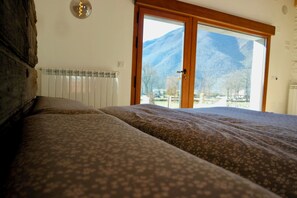 A bedroom with a bed, a wooden headboard, a window with a view of mountains, and a radiator. - Quiet design duplex with mountain views (Villablino)