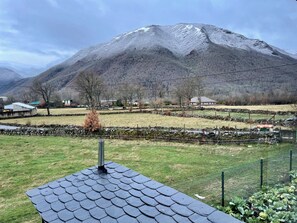 A rural landscape with a mountain, stone walls, and a fenced area with vegetation.