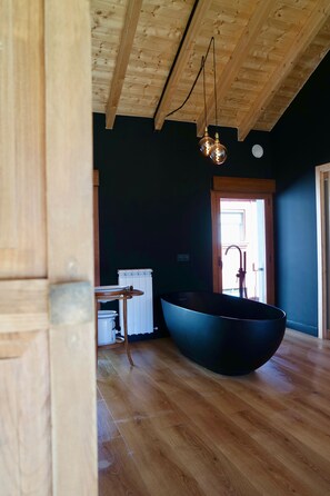Un interno moderno con una grande vasca da bagno nera, pavimento in legno e soffitto in legno.