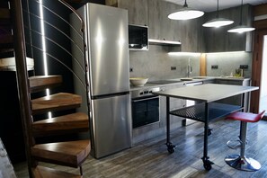 A modern kitchen with a built-in oven, a stainless steel refrigerator, and a wooden staircase.