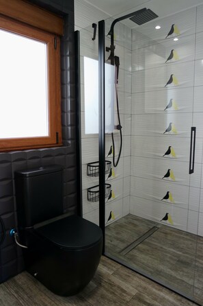 A bathroom with a black toilet, a shower with a black hose, and a tiled wall with bird patterns. - Quiet design duplex with mountain views (Villablino)