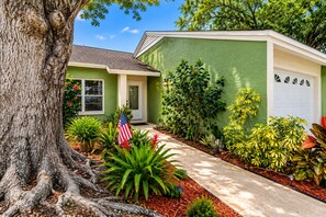 A residential house with a green exterior, a driveway, and a large tree in the foreground. - Tropical Largo Pool House Near Beaches | Private Pool Retreat (Largo)