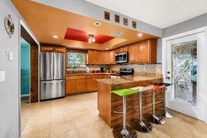 A modern kitchen with wooden cabinets, stainless steel appliances, a central island with bar stools, and a decorative glass door. - Tropical Largo Pool House Near Beaches | Private Pool Retreat (Largo)