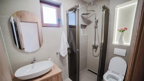 Een badkamer met een houten wastafelmeubel, een witte wasbak, een douchecabine van glas en een toilet.