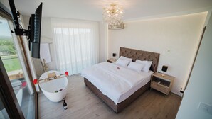Een slaapkamer met een groot bed, een badkuip, een kroonluchter en uitzicht op de omgeving.