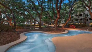 A swimming pool with a wavy design, surrounded by trees and a building in the background. - Resort with 2 bedrooms and AC in beautiful Marriott Grande Ocean (Hilton Head Island)