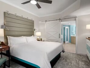 Una camera d'albergo con un letto, comodini, una ventola a soffitto e una porta scorrevole che dà su un bagno.