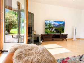 A living room with a television, a fireplace, and a view of a garden through glass doors.