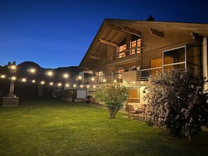 Una casa de dos pisos con balcón, césped y luces colgantes.