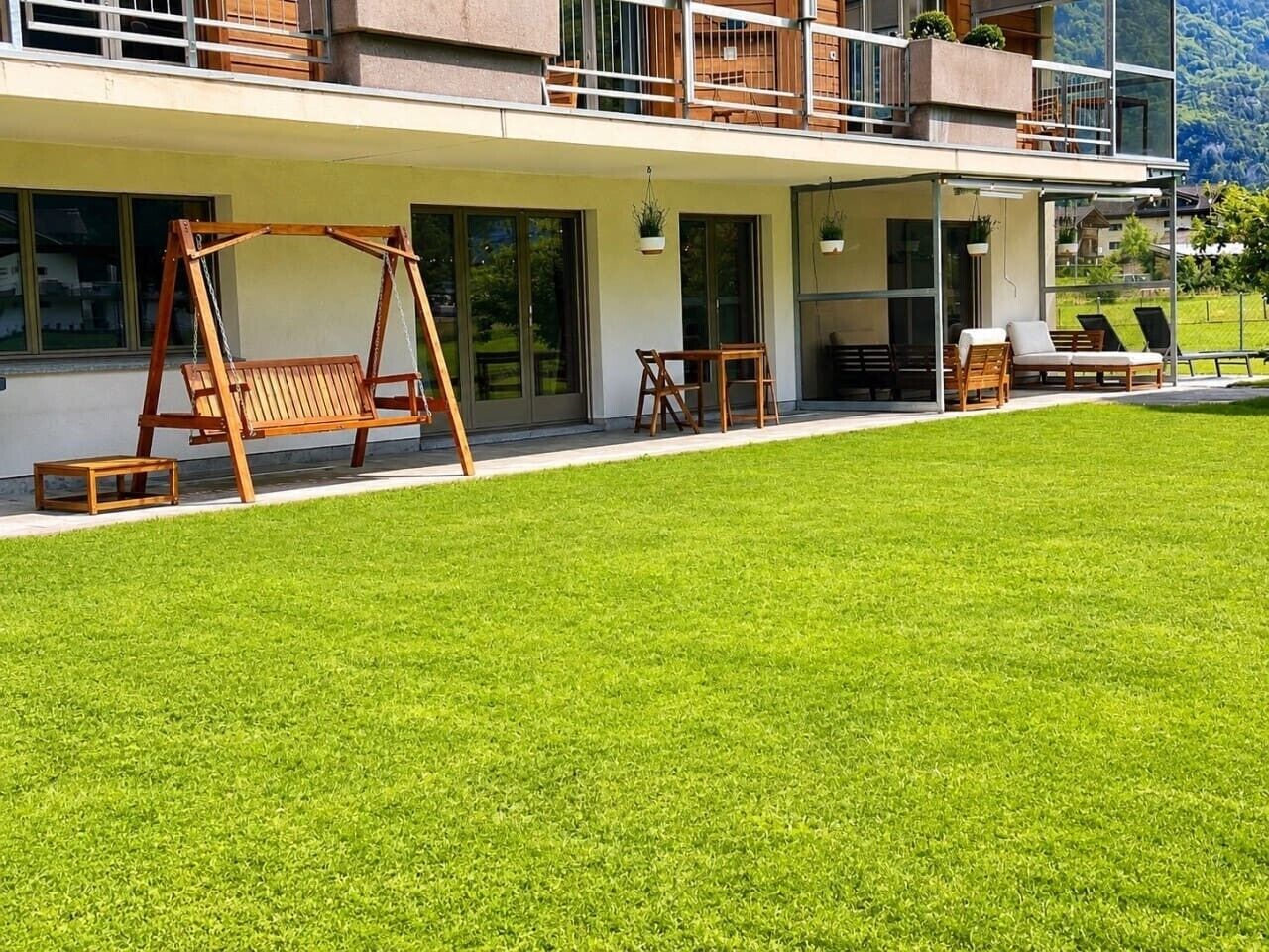 Ein modernes Haus mit gepflegtem Rasen, Sitzgelegenheiten im Freien und einem Balkon mit Blick.