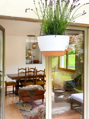 Un intérieur moderne agrémenté d’un pot de fleurs suspendu, d’un coin repas avec des meubles en bois et d’une porte vitrée donnant sur un espace extérieur.
