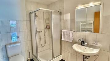 A bathroom with a glass-enclosed shower, a toilet, a sink with a mirror, and a towel hanging on the wall.