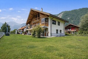 A two-story building with a balcony, a grassy yard, and a mountain backdrop.