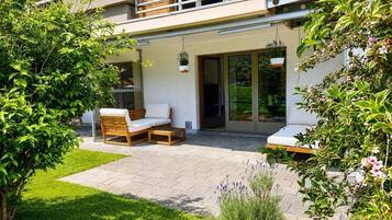 Een modern huis met een terras, buitenmeubilair en een glazen entree.