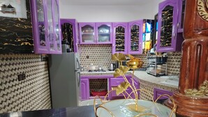 Eine Küche mit violetten Schränken, einer Marmor-Spritzschutzwand und einer goldenen Zimmerpflanze auf der Arbeitsfläche.