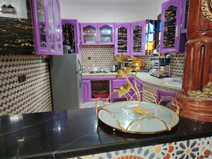 Eine Küche mit violetten Schränken, einer Marmor-Spritzschutzwand und einer goldenen Zimmerpflanze auf der Arbeitsfläche.