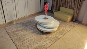 Ein Zimmer mit einem runden, mehrstufigen weißen Tisch, einer Couch, einem gemusterten Teppich und einer Tür mit Griff.