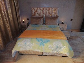 Ein Bett mit floralem Überwurf, ein Kopfteil mit Rautenmuster und zwei Nachttische mit Lampen.