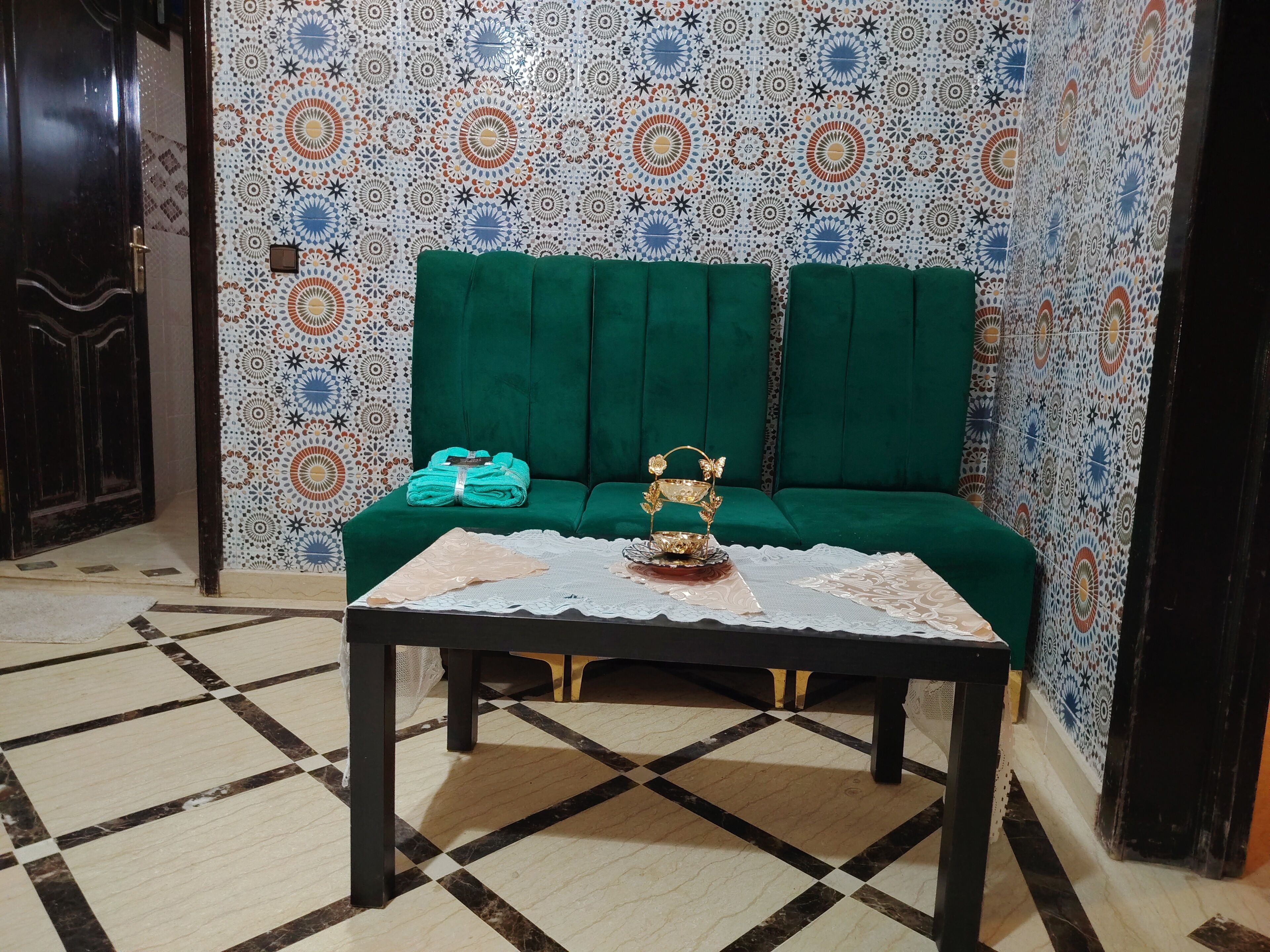 A room with a green sofa, a table with a lace tablecloth, and patterned wallpaper.