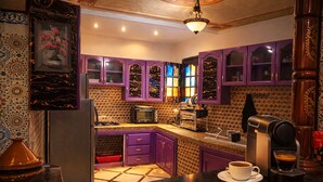 Eine Küche mit violetten Schränken, einer Mikrowelle, einer Kaffeemaschine und einer gefliesten Spritzschutzwand.