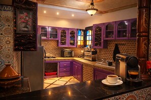 Eine Küche mit violetten Schränken, einer Mikrowelle, einer Kaffeemaschine und einer gefliesten Spritzschutzwand.