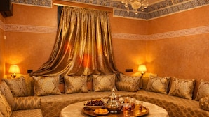 Ein luxuriöses Zimmer mit einer Sofagarnitur, einem runden Tisch mit einer Tafel mit Speisen und Getränken sowie einer Chandelier.