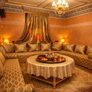 Ein luxuriöses Zimmer mit einer Sofagarnitur, einem runden Tisch mit einer Tafel mit Speisen und Getränken sowie einer Chandelier.