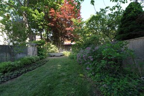 A backyard with a lawn, a wooden fence, and a variety of plants and trees. - Upscale Historic West End Townhouse with Expansive Garden (Portland)